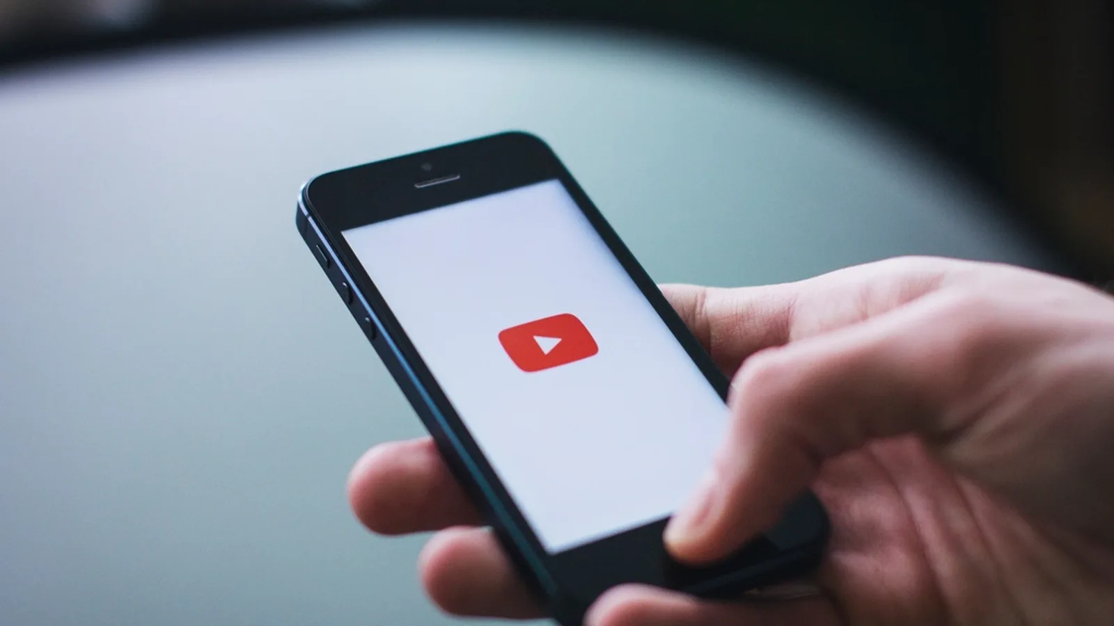 Hand holding a smartphone with the YouTube mobile app visible on screen